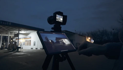 Tablet mounted on tripod displaying video footage during twilight outdoor shoot at commercial building.