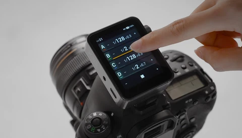 Hand touching smartphone screen displaying camera exposure settings mounted on DSLR camera body.
