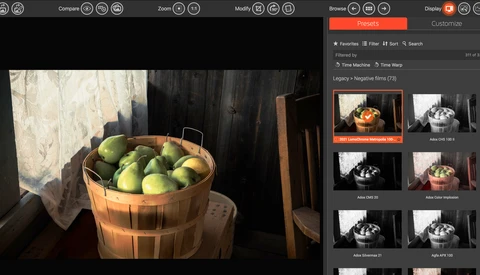 Wooden bushel basket filled with green apples, backlit by window light with dramatic shadows.