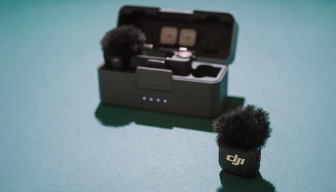 DJI wireless microphone with windscreen next to its charging case on a blue background.