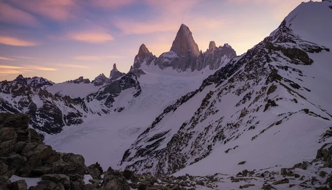 Snow-covered peaks at sunrise with jagged granite spires rising above an alpine glacier.