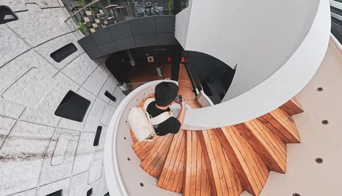 Overhead view of a curved staircase with wooden treads descending into a dark interior space.