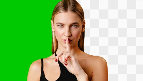 Woman with reddish-blonde hair making a shushing gesture with her finger to her lips.