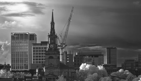 Urban skyline in black and white showing a church spire amid modern office buildings and a construction crane.