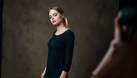 Woman in black long-sleeve shirt posed against textured neutral background.