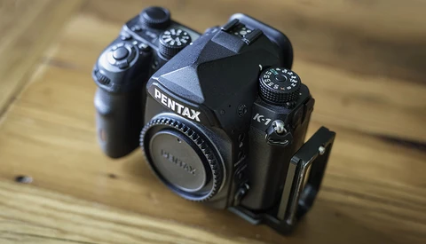 Two Pentax film cameras positioned on a wooden surface, showing K-7 and K-x models with manual lens focus rings.