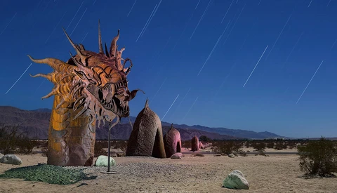 Large wooden dragon sculpture with elaborate carved details stands in a desert landscape under a starry night sky.