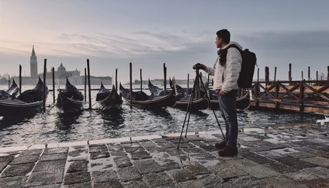 Photographer with tripod overlooking Venetian gondolas and historic architecture at dawn.