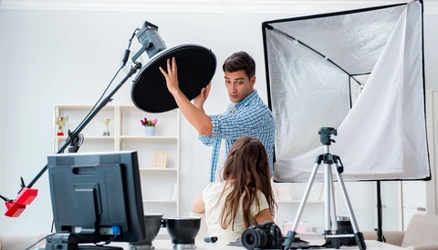 Two people adjusting a large softbox light modifier in a home photography studio setup.
