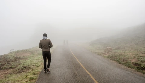 Runner jogging solo on a misty mountain road with yellow center line.
