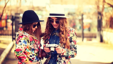 Two women wearing colorful floral blazers and sunglasses standing outdoors in a park.