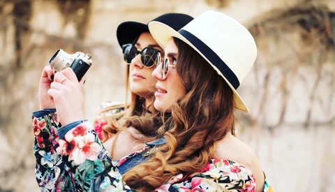 Woman in floral jacket and white Panama hat holding vintage film camera to her face.
