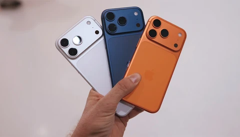 Three smartphone cases in white, dark blue, and orange held in a hand, displaying triple-lens camera modules.