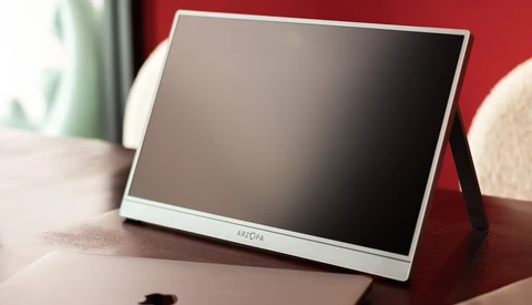 Portable monitor with white bezel and stand displayed on a desk with red background.