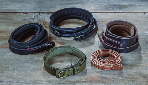 Five leather camera straps in different colors and styles arranged on weathered wood.