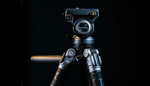 Professional video camera tripod head mounted on carbon fiber legs against a black background.