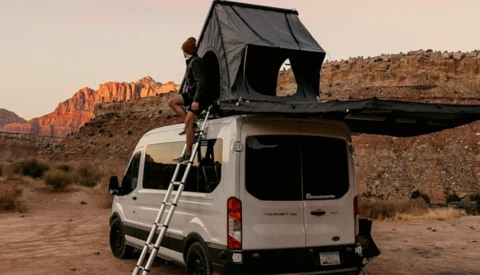 White van with open roof tent in desert landscape during golden hour.