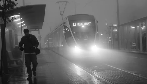 Runner in dark clothing passing an illuminated tram on a wet platform shrouded in fog.