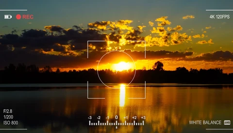 Camera viewfinder displaying a golden sunset reflected in still water with exposure and white balance controls visible.