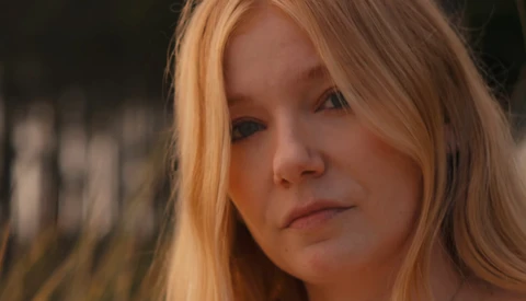 Woman with long reddish-blonde hair gazing downward with a contemplative expression.