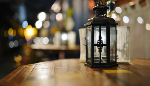 Black metal lantern with glass panels and lit candle on wooden table at night.