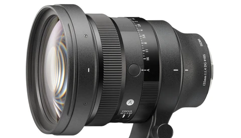 Professional camera lens with optical elements visible through front glass, mounted on a black support base against white background.