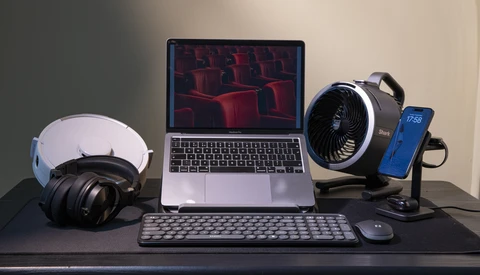 Creative workspace setup with laptop, headphones, microphone, keyboard, and phone on dark desk.