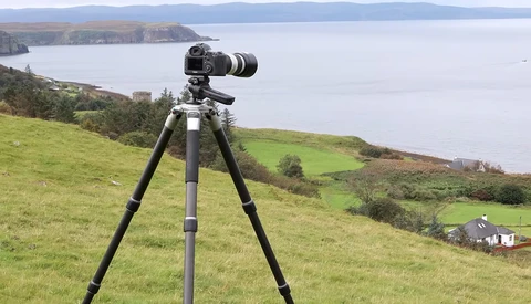 Camera mounted on tripod overlooking coastal landscape with mountains and water.