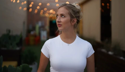 Woman in white t-shirt looking upward in indoor setting with warm bokeh lighting.