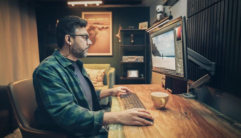 Creative professional editing photos on a desktop computer in a warm-lit home studio setup.