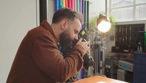 Photographer looking through camera viewfinder in studio with professional lighting setup.