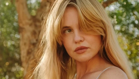 Young woman with long blonde hair gazing over shoulder in natural outdoor setting.