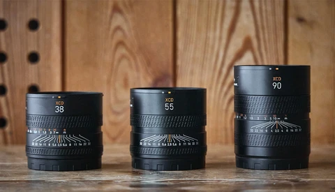 Three black camera lenses with focal lengths 38mm, 55mm, and 90mm arranged in a row on a wooden surface.