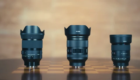 Three camera lenses of varying sizes arranged side by side on a reflective surface against a warm, blurred background.