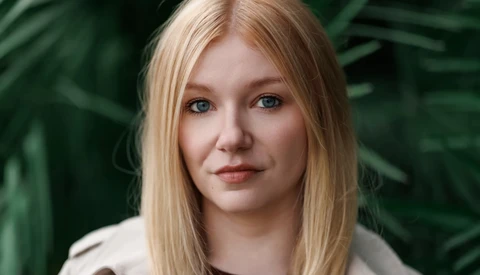 Portrait of a woman with straight blonde hair against blurred green foliage background.