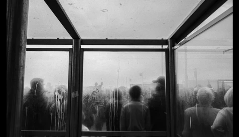 Silhouetted figures visible through rain-streaked windows with dark structural framing.
