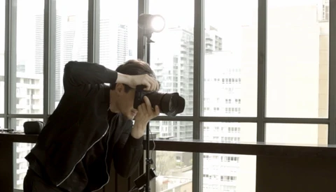 Photographer shooting with a telephoto lens from a high-rise window overlooking a city skyline.