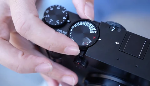 Close-up of a photographer's hand adjusting the exposure compensation dial on a black camera body.
