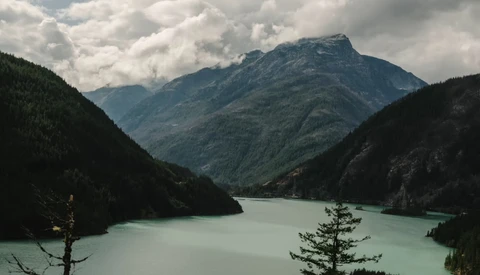 Alpine lake with turquoise water surrounded by forested mountains and dramatic cloudy sky.