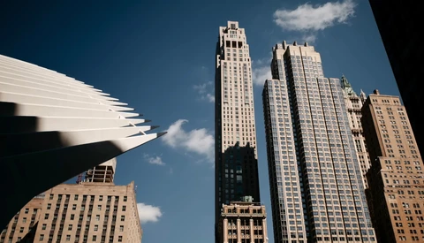 Upward view of modern and historic skyscrapers against a bright blue sky with white clouds.