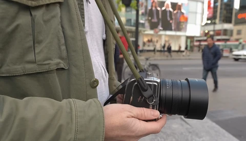 Photographer holding a mirrorless camera with telephoto lens on a city street.