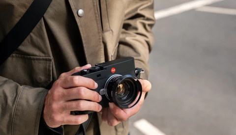 Photographer holding a rangefinder camera with a bright lens element visible in daylight.