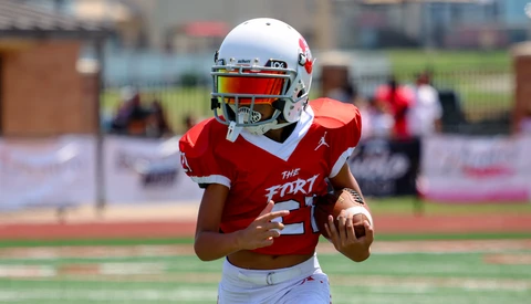 Young football player in red jersey running with the ball during a daytime game.