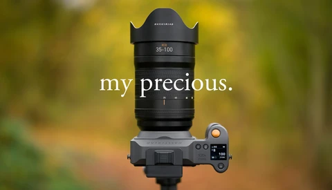 Hasselblad 35-100mm zoom lens mounted on a mirrorless camera body against a blurred green and yellow background.
