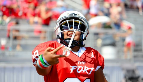 Football player in red jersey pointing toward camera during daytime stadium game.