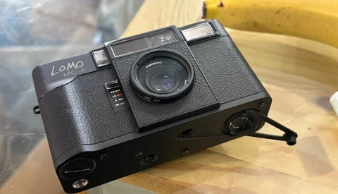 Lomo compact film camera with textured black body and manual controls positioned on wooden surface.