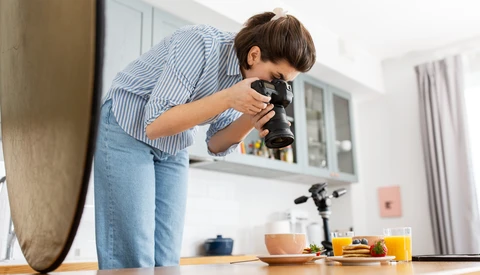 Photographer composing a still life shot of kitchen items on a wooden table using a professional camera.