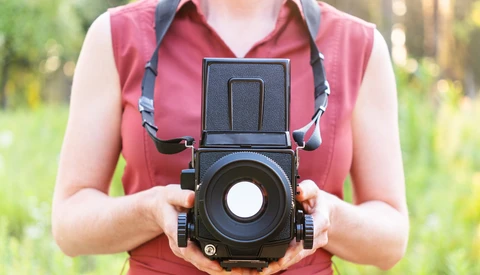 Photographer holding a medium format camera with flip-up viewfinder against their body.