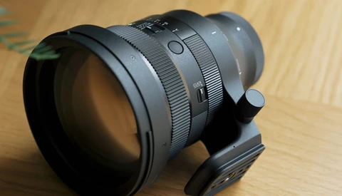Fast telephoto lens with focus ring and depth-of-field markings mounted on wooden surface.