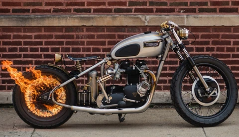 Custom motorcycle with flame design on front wheel, silver fuel tank, and black engine against brick wall.